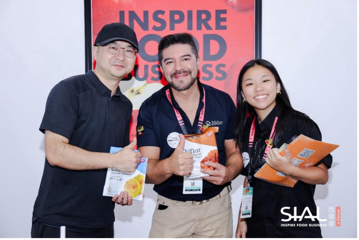 Exhibitors holding snack products and giving thumbs-up at SIAL photo backdrop