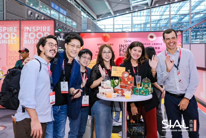 Diverse group of cheerful attendees waving around a cocktail table at SIAL exhibition