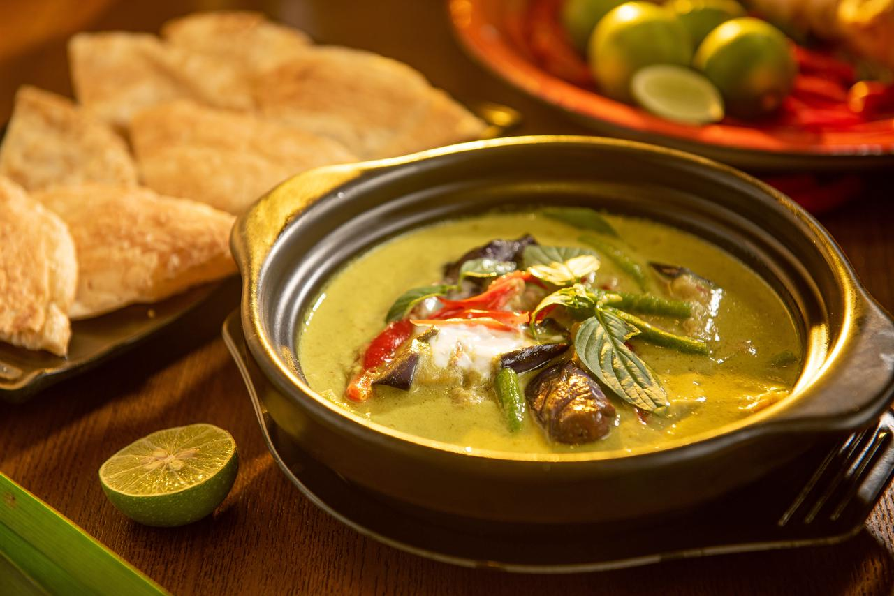 A flavorful Thai green curry with vegetables and aromatic herbs in a stylish black bowl
