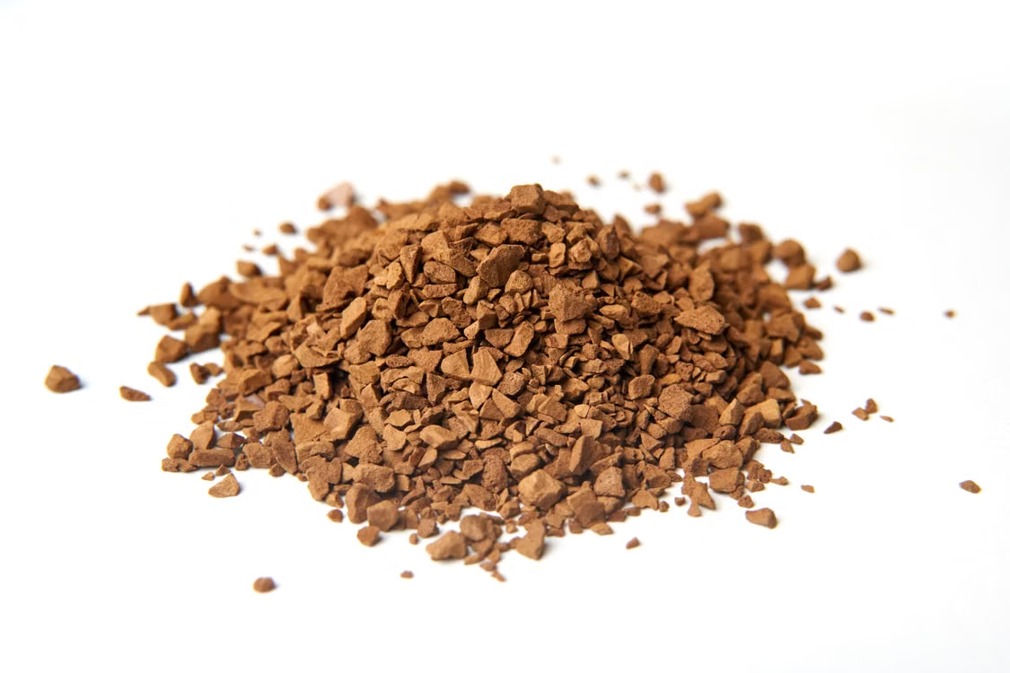 Macro shot of coarse brown coffee granules piled on a clean white background, perfect for caffeine lovers