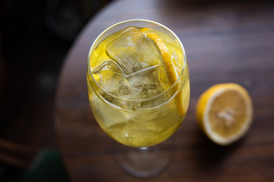 Chilled citrus beverage in a wine glass with ice cubes and lemon slice on a wooden table.