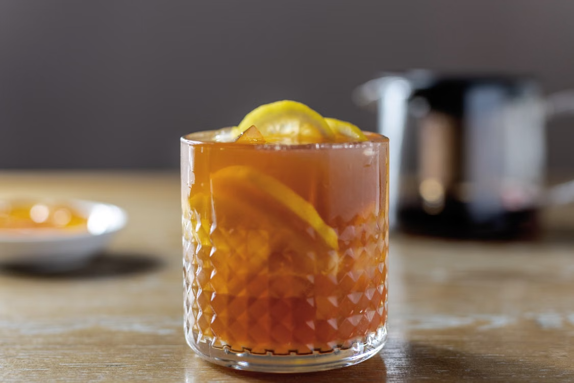 A close-up of a refreshing iced tea with lemon slices in a textured glass on a wooden table.