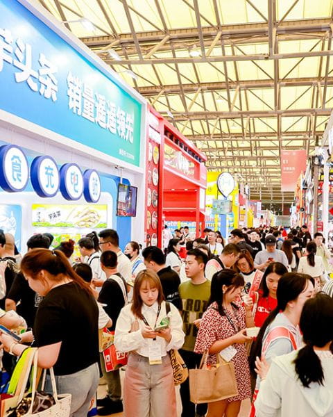 Crowded exhibition hall with visitors exploring colorful booths at a food trade show in Shanghai.